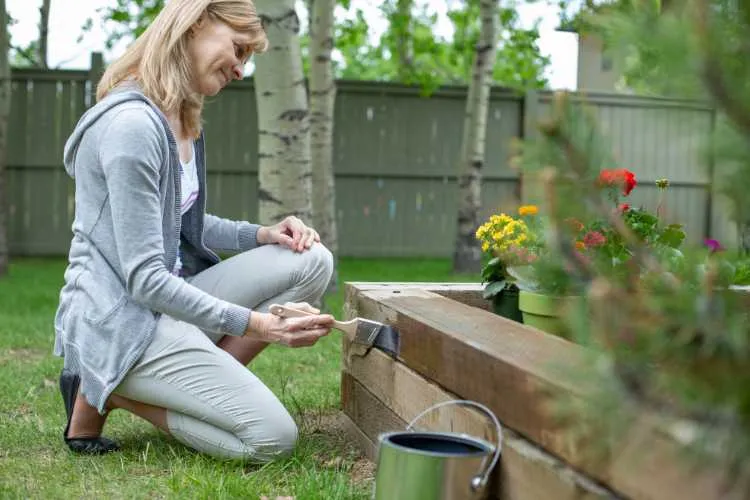 woman painting wood on raised flower bed
